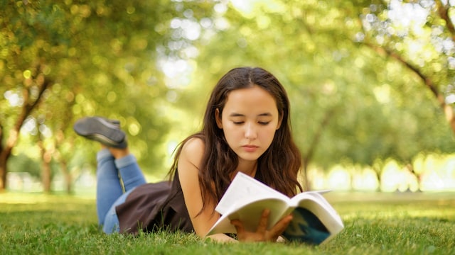 Chica adolescente leyendo un libro tumbada en el césped en verano