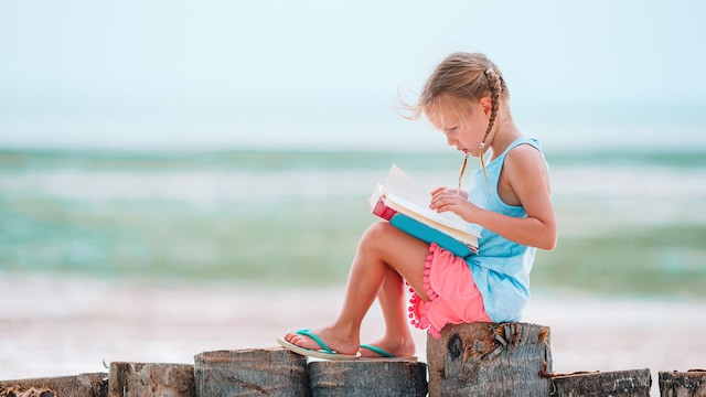 Niña pequeña leyendo un libro con el mar al fondo