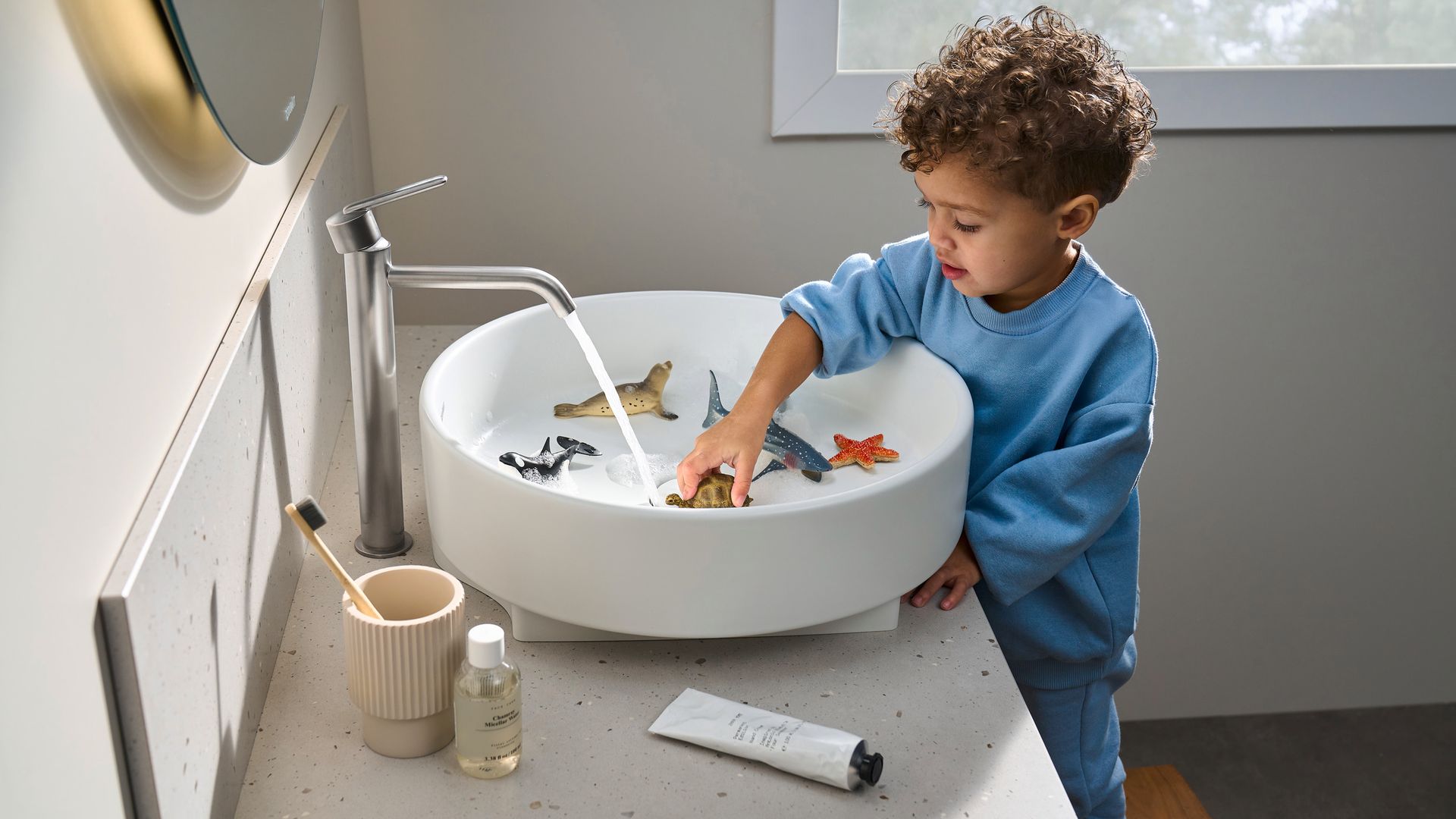 Niño jugando en el lavabo, con muñecos de goma, accesorios para el cepillo de dientes