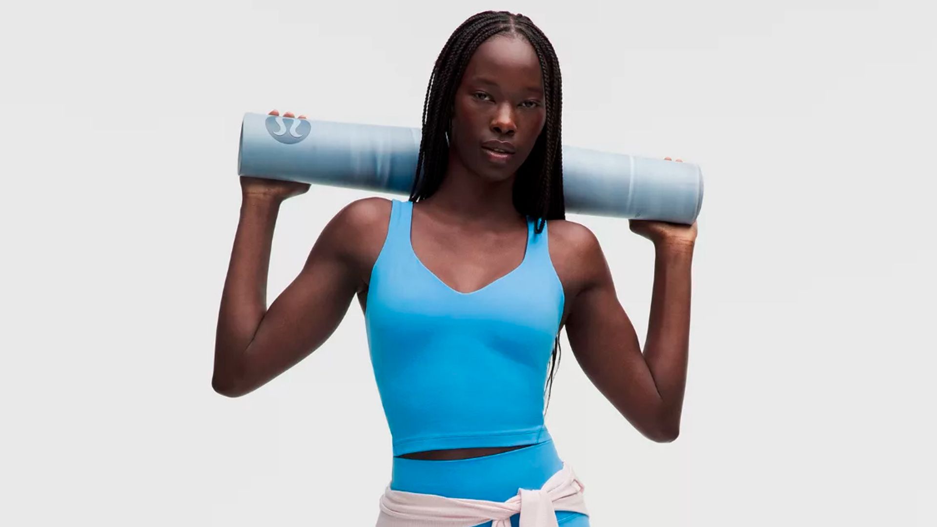 Mujer con conjunto de deporte corto y azul de lululemon, sujetando una esterilla sobre los hombros