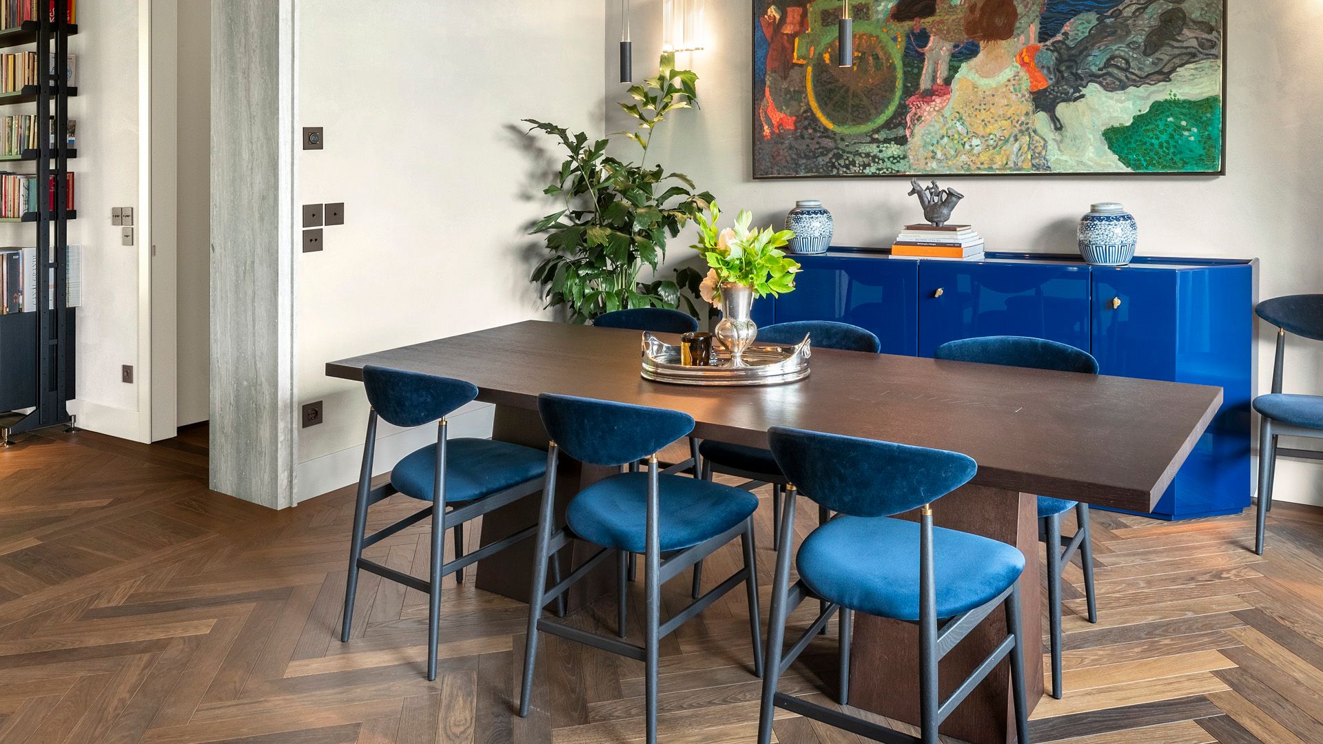 Comedor con mesa de madera oscura, aparador azul eléctricos, sillas tapizadas en azul oscuro, suelo de madera oscura