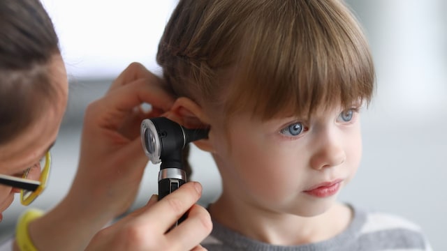 Niña en la consulta del otorrino mientras la explora con el otoscopio por otitis