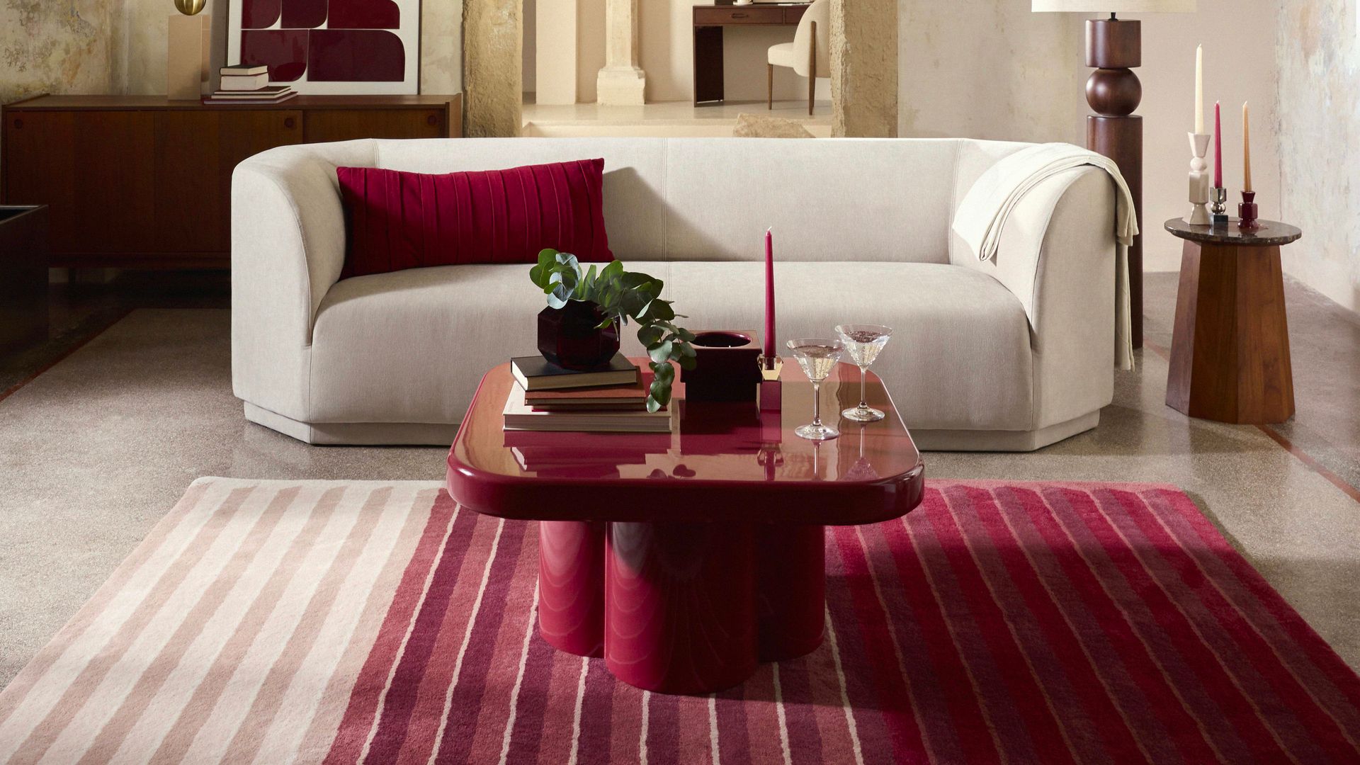 Salón con sofá blanco, cojín rojo, alfombra de color burdeos, mesa de centro lacada en color rojo, lámpara de pie