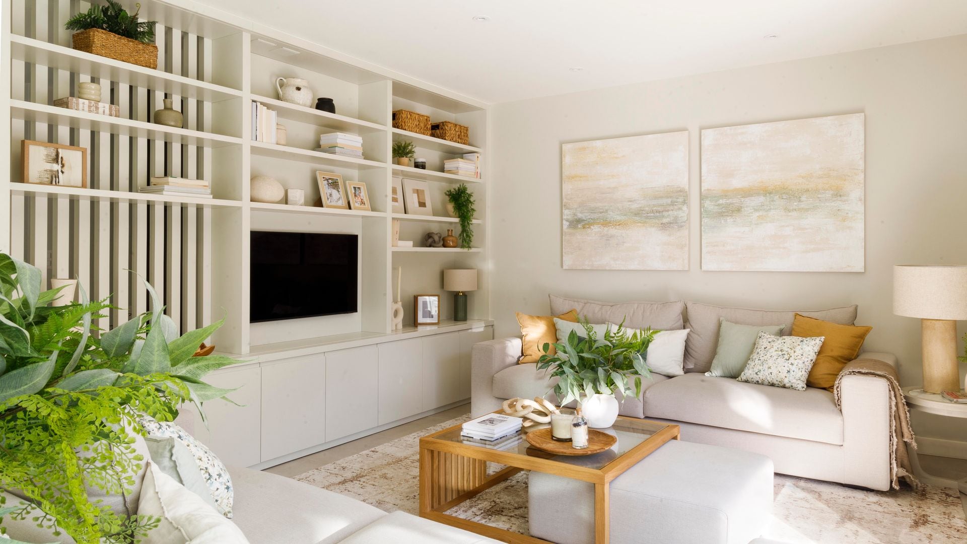 Salón con estantería a medida, con hueco para la televisión, sofás blancos, cuadros en la pared, mesa de centro de madera, puff blanco bajo la mesa de centro, adornos y fotos, alfombra