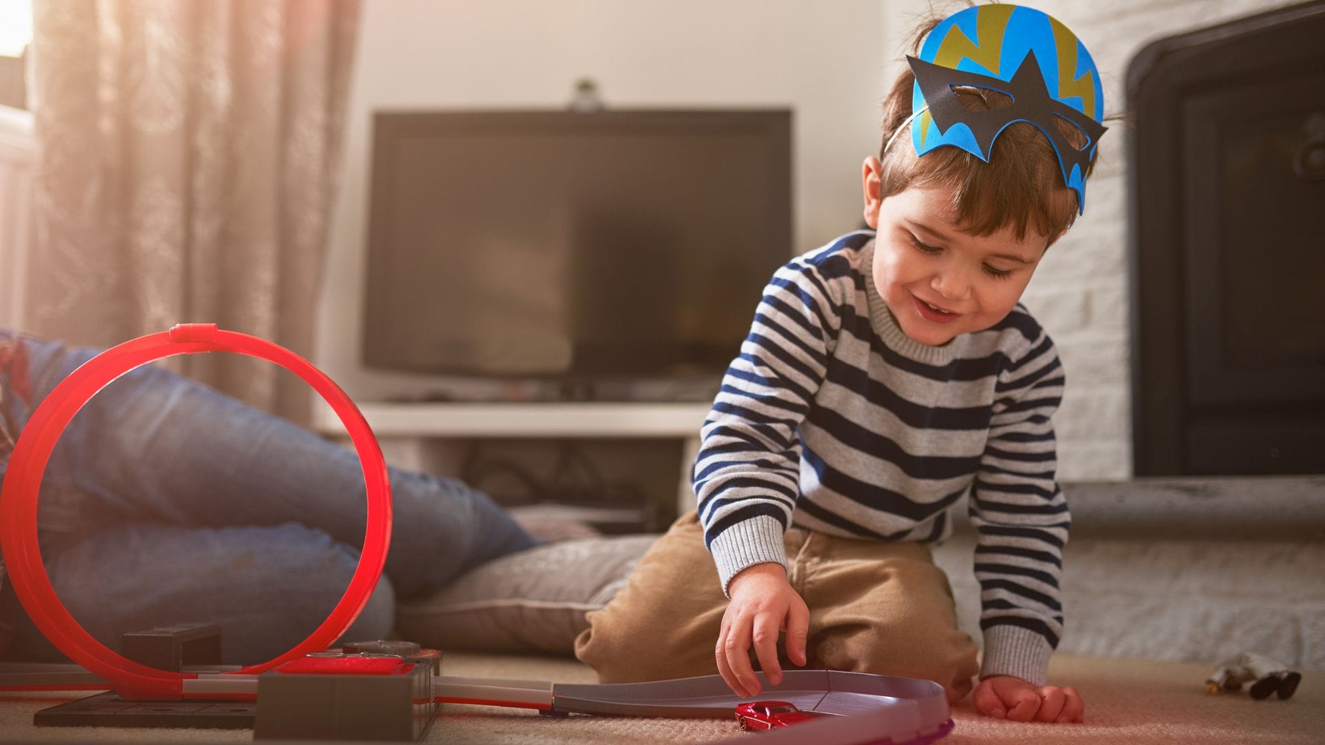 Niño jugando con una pista de coches con una máscara de cartulina en la cabeza.