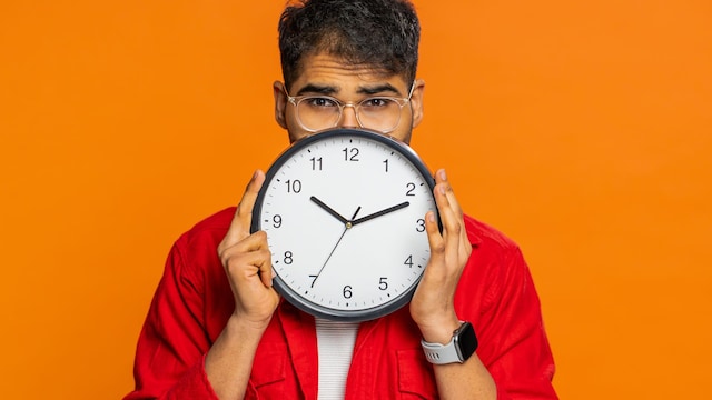 Un hombre esconde su cara detrás de un reloj que marca las 10:10