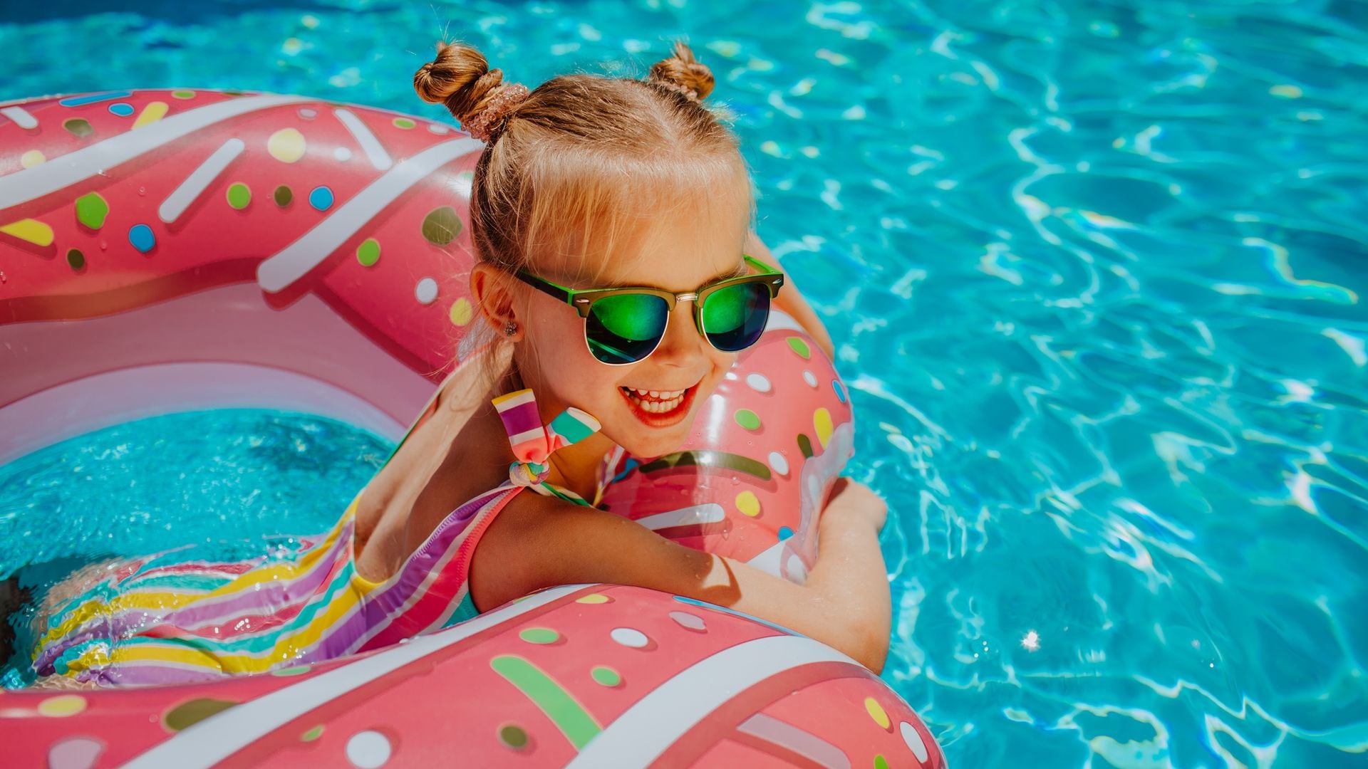 Niña con gafas de sol sobre un flotador en la piscina