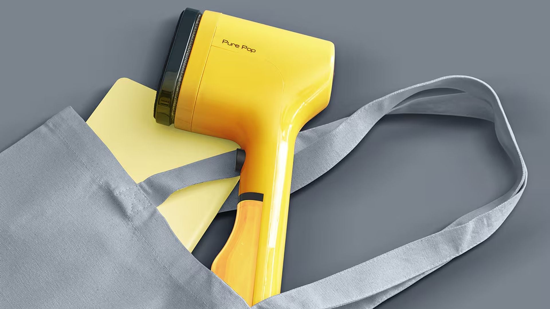 Plancha de vapor vertical en amarillo, dentro de un bolso con otros accesorios del mismo color. Fondo gris.