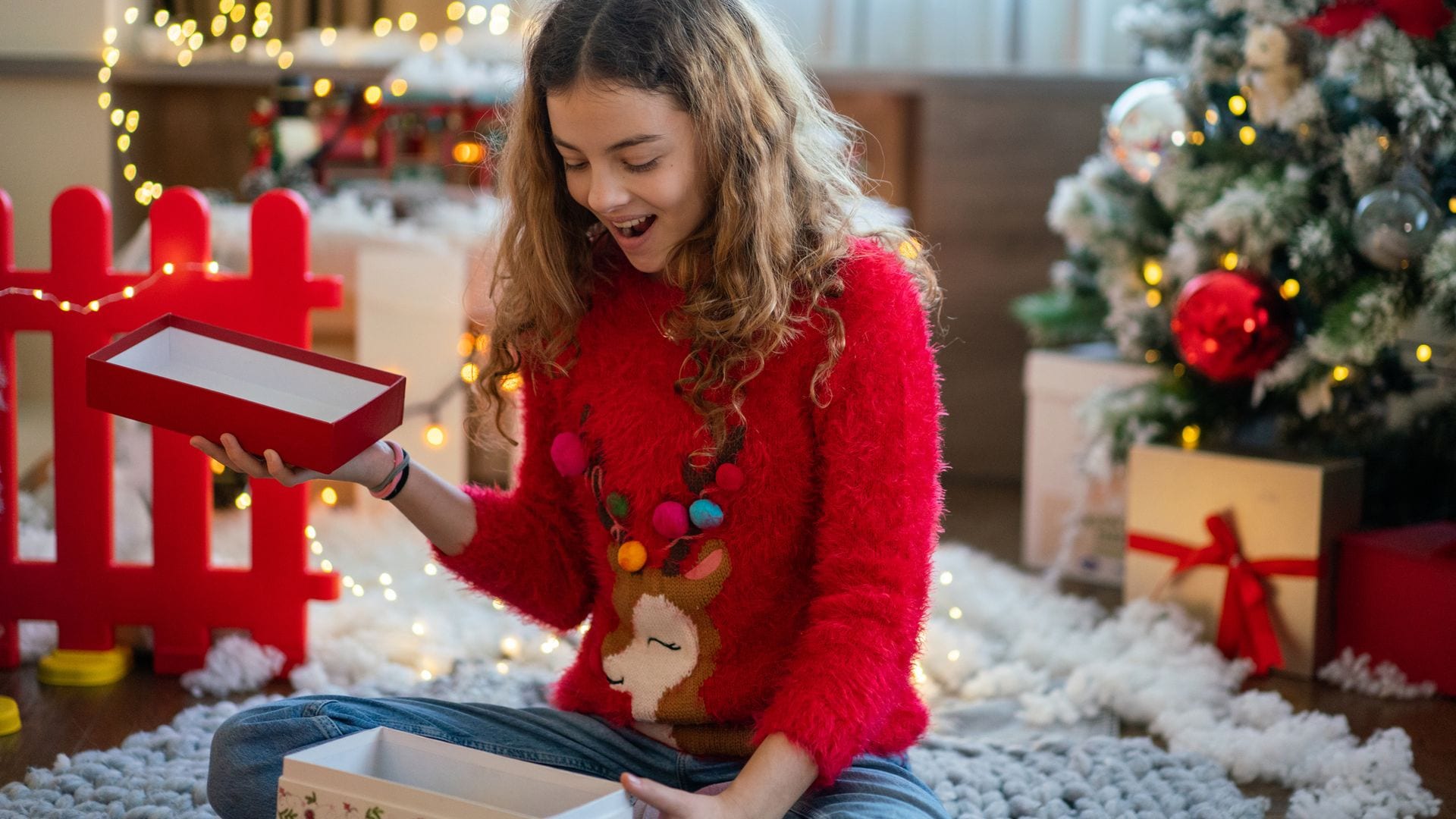 Niña adolescente abriendo un paquete de Navidad en casa, sonriendo, con un jersey navideño