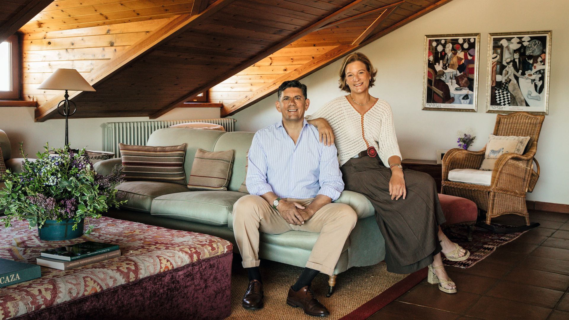 Silvia y su marido, Luis, en el salón abuhardillado de la planta superior, con techos y vigas de madera natural, que cuenta con diversas zonas de descanso que combinan sofás de diferentes colores y estampados, mesas de centro y un gran tragaluz que llena el espacio de luz natural
