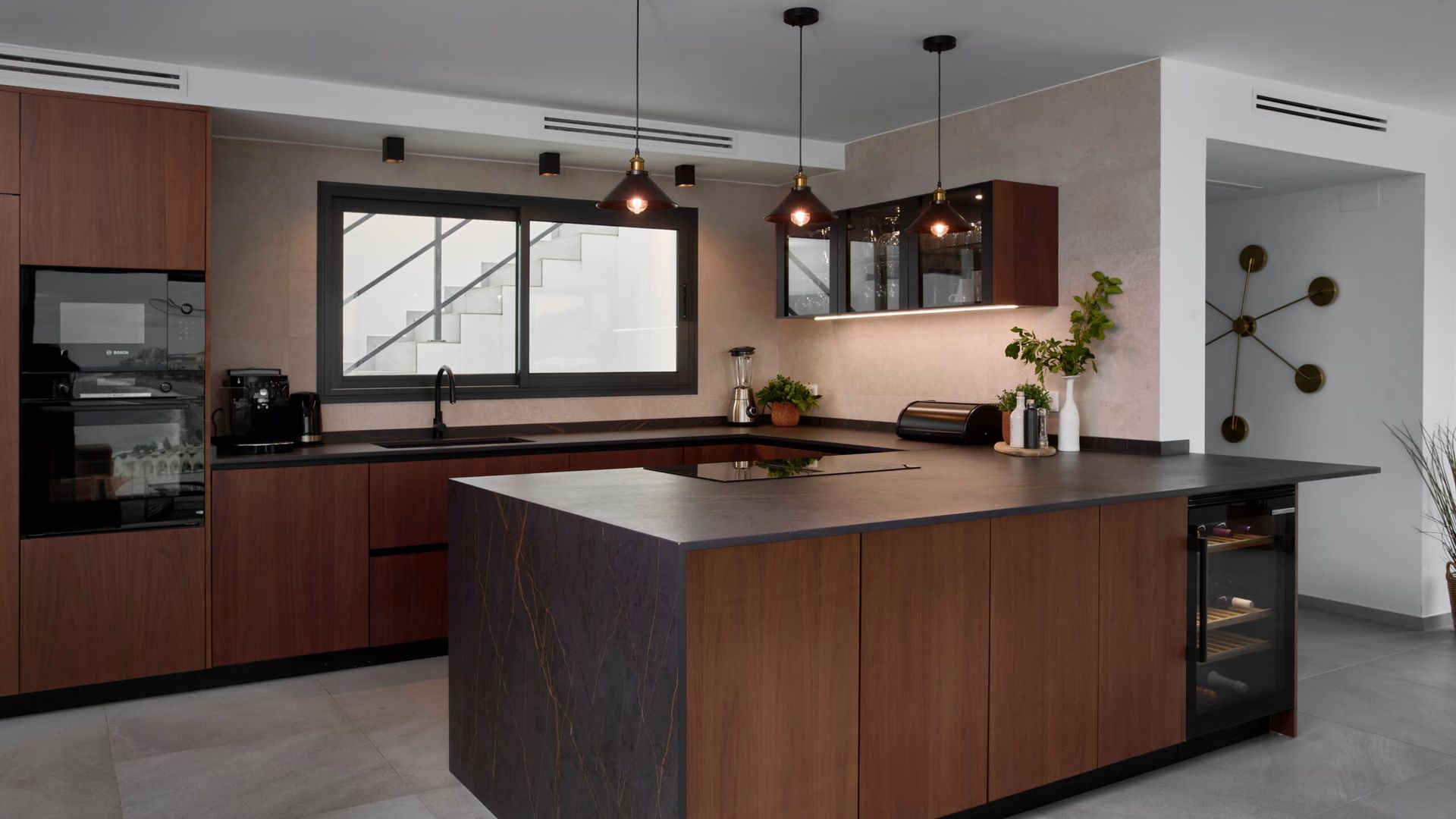 Cocina con península con muebles de madera oscura, vinoteca bajo la península, encimera negra 