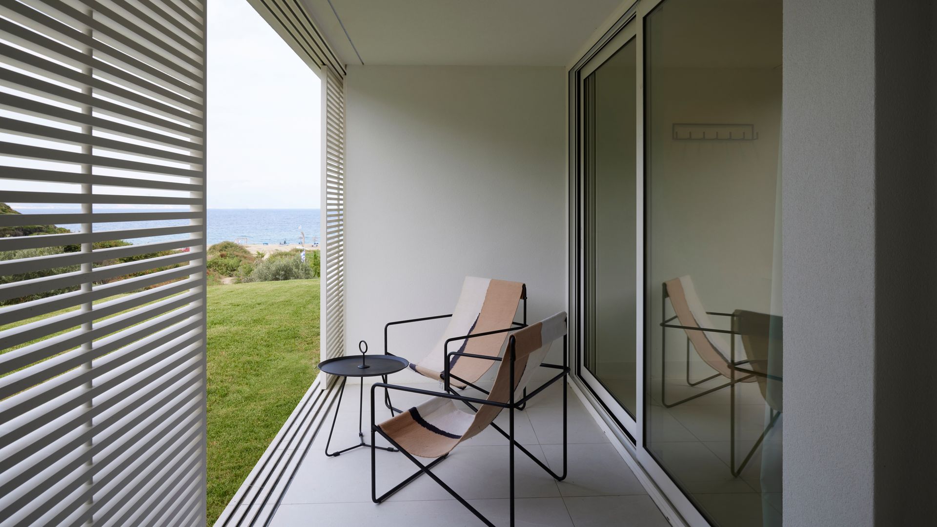 Terraza con cerramiento de lamas de madera blancas, butacas de cuero y mesa auxiliar negra 