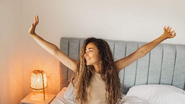 Mujer con pelo rizado estirándose en la cama, levantándose descansada y sonriente