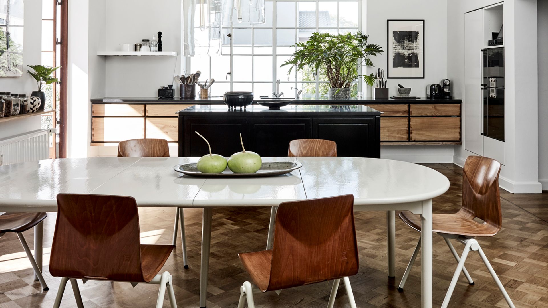 Cocina abierta al comedor, muebles de cocina de madera oscura, isla negra, suelo de madera, lámparas de techo sobre la mesa blanca de comedor 
