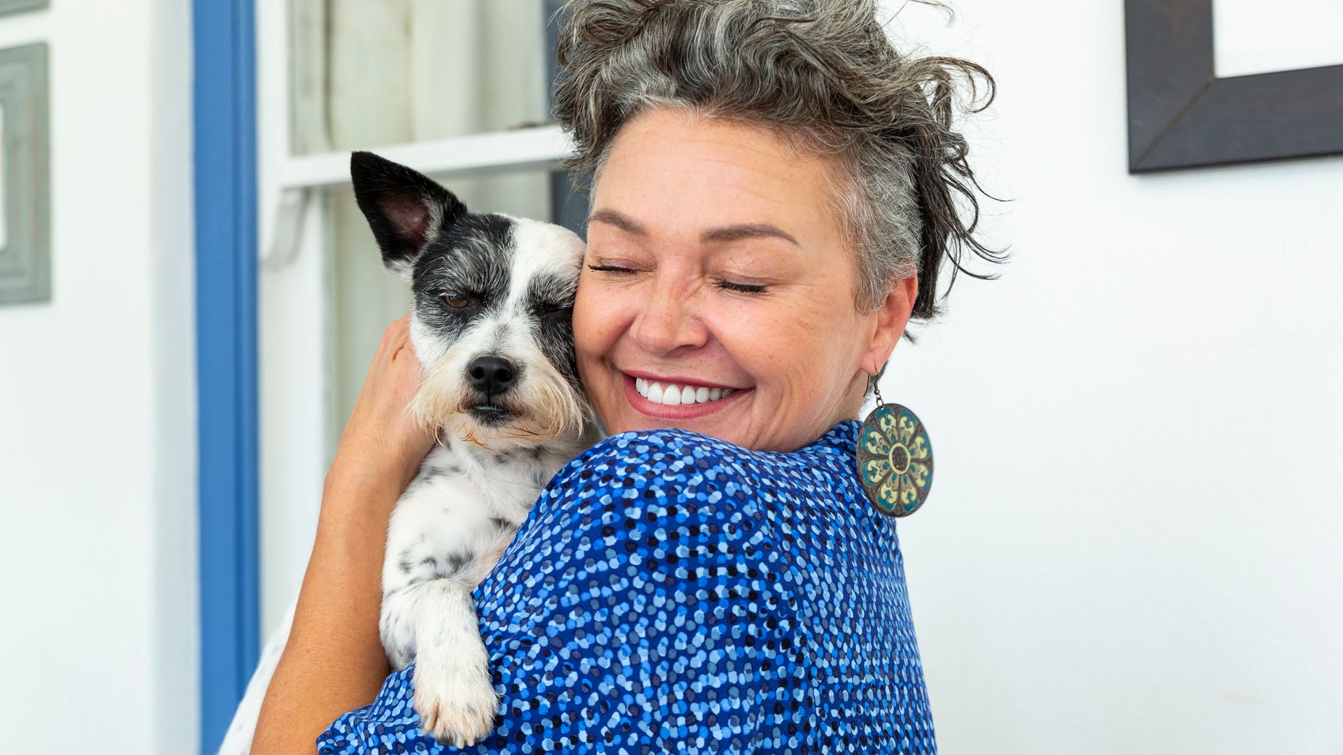 Mujer madura feliz con pelo corto abrazando a un perro en casa