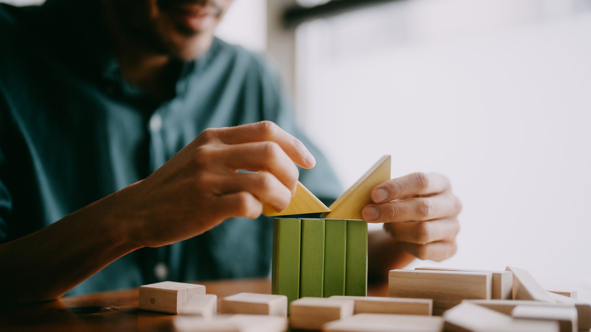 Hombre jugando con un juego de lógica de bloques de madera en una mesa.