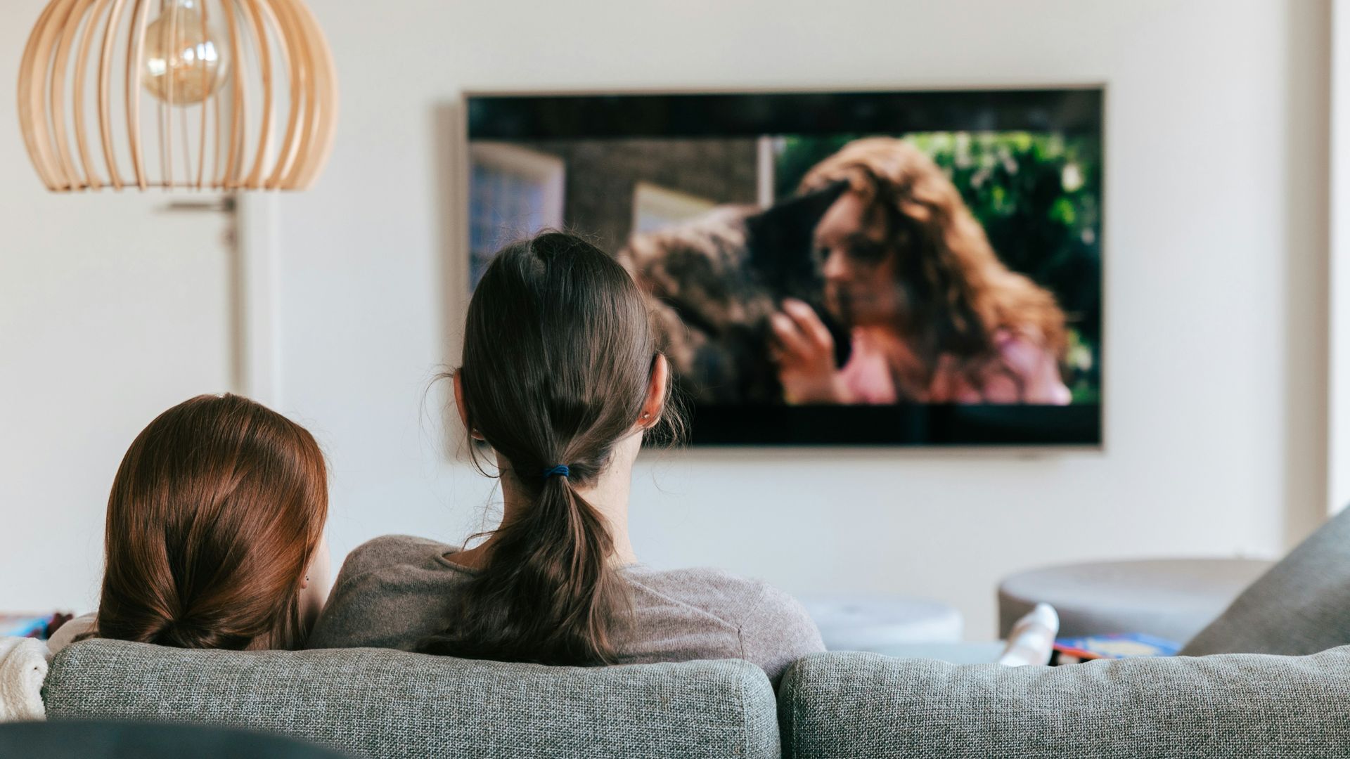 Madre e hija viendo la televisión en el sofá de su casa, de espaldas a la cámara