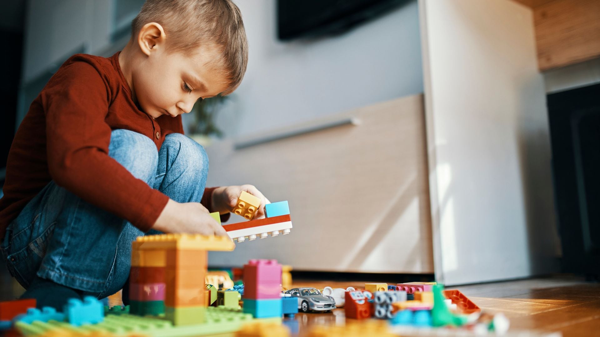 Niño jugando con bloques de construcciones en el suelo de una habitación.