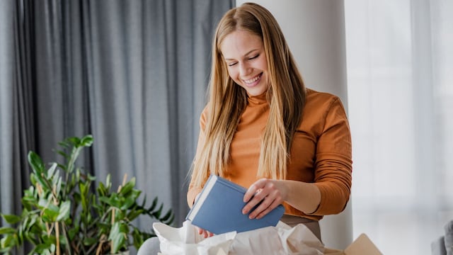 Mujer alegre con una camiseta naranja abriendo cajas de paquetes
