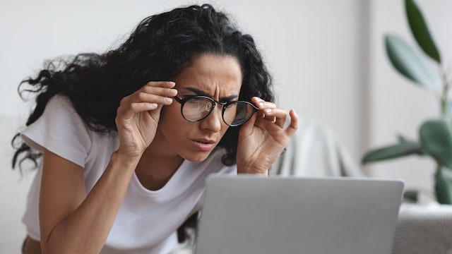 mujer joven ajustándose las gafas mientras mira el ordenador