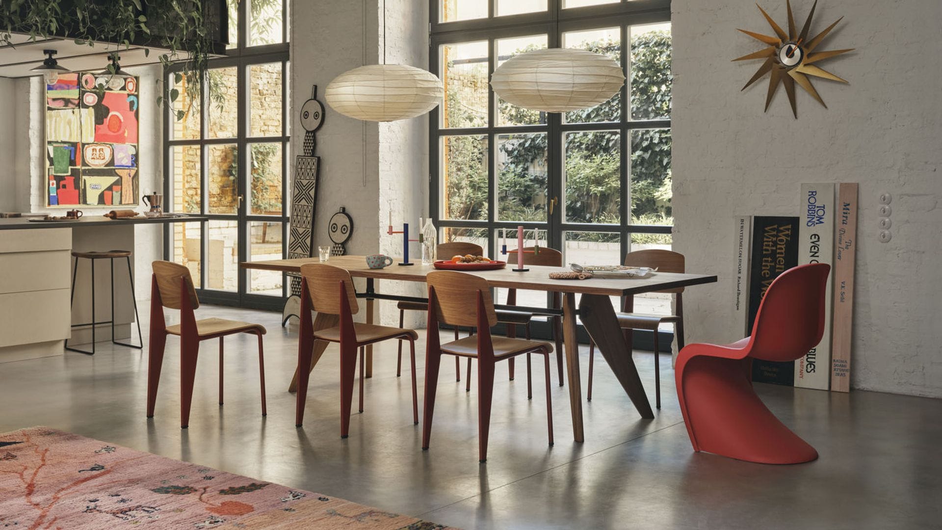 Comedor con lámparas de techo de papel, sillas Panton roja, sillas de madera, espejo dorado en la pared, grandes ventanales con salida al jardín,  mesa de madera