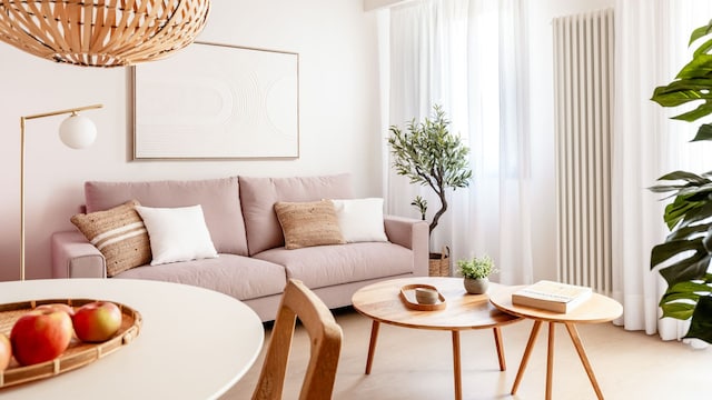 Salón comedor con vigas de madera en el techo, sofá rosa palo, lámpara de techo de fibras vegetales, mesas de centro de madera, plantas, suelo de madera 