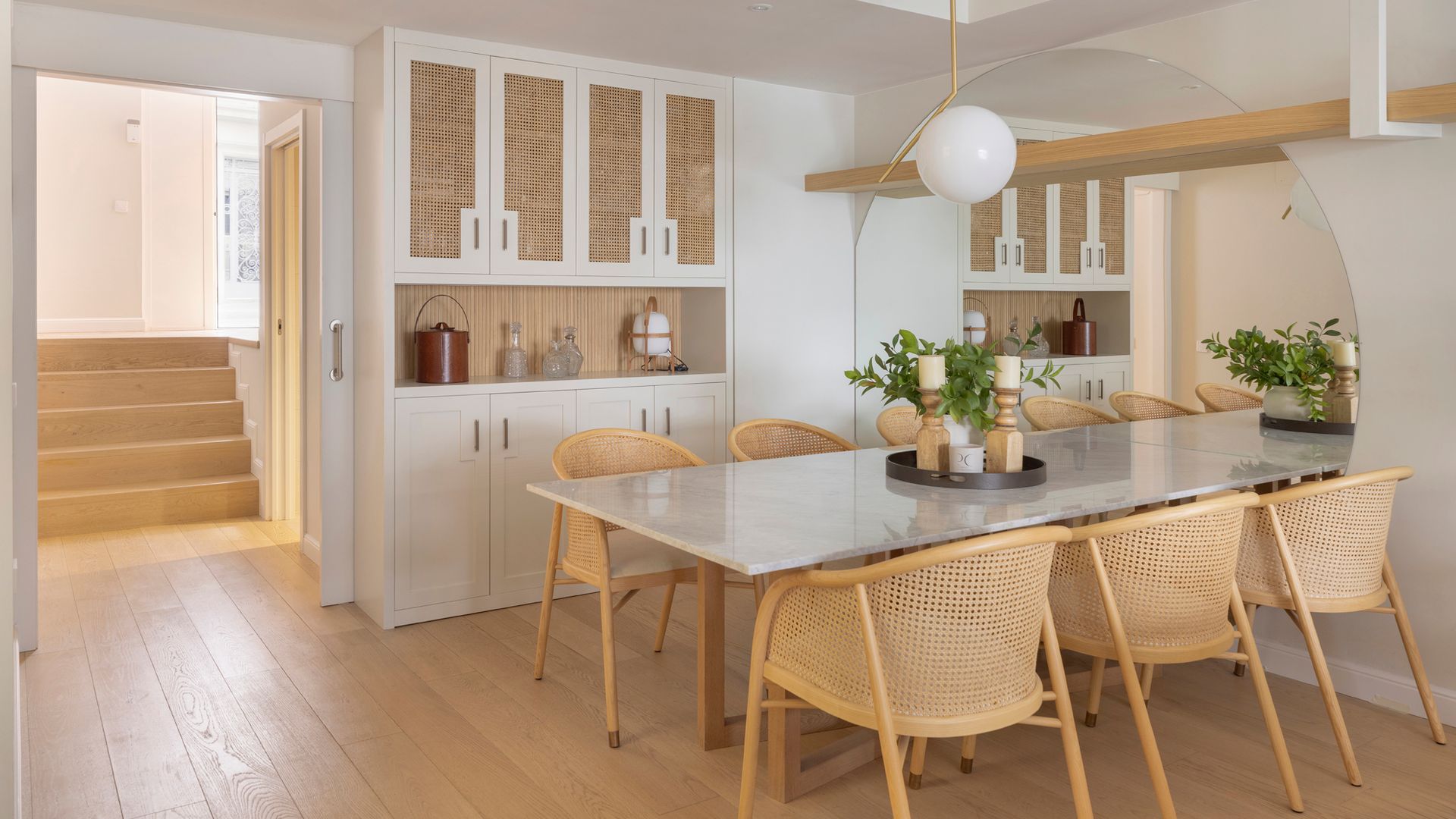 Comedor con asientos, de rejilla lámpara de techo con bola blanca, suelo de madera, mueble blanco con puertas de rejilla y armarios en la parte inferior