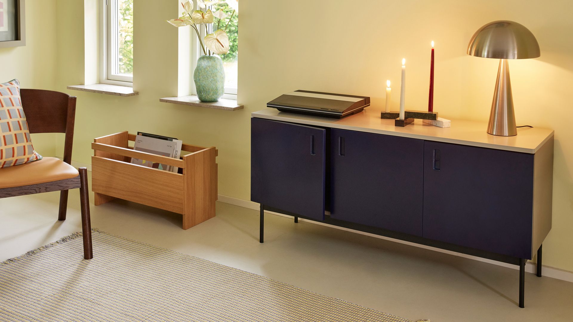 Rincón del salón con aparador azul, velas encendidas, lámpara de sobremesa dorada, revistero de madera