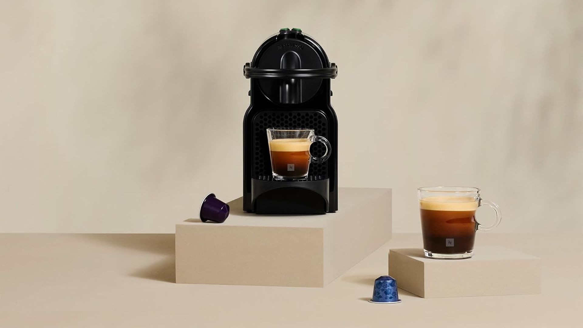 Cafetera Nespresso De'Lomghi en un montaje 'beige' con cápsulas y tazas de café.