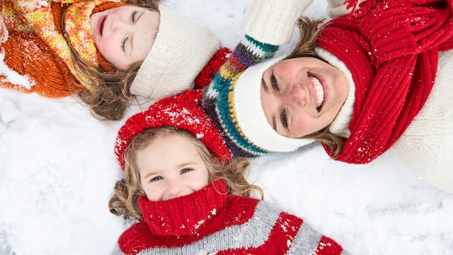 Madre con sus hijos riéndose en la nieve en invierno con guantes, gorros y bufandas