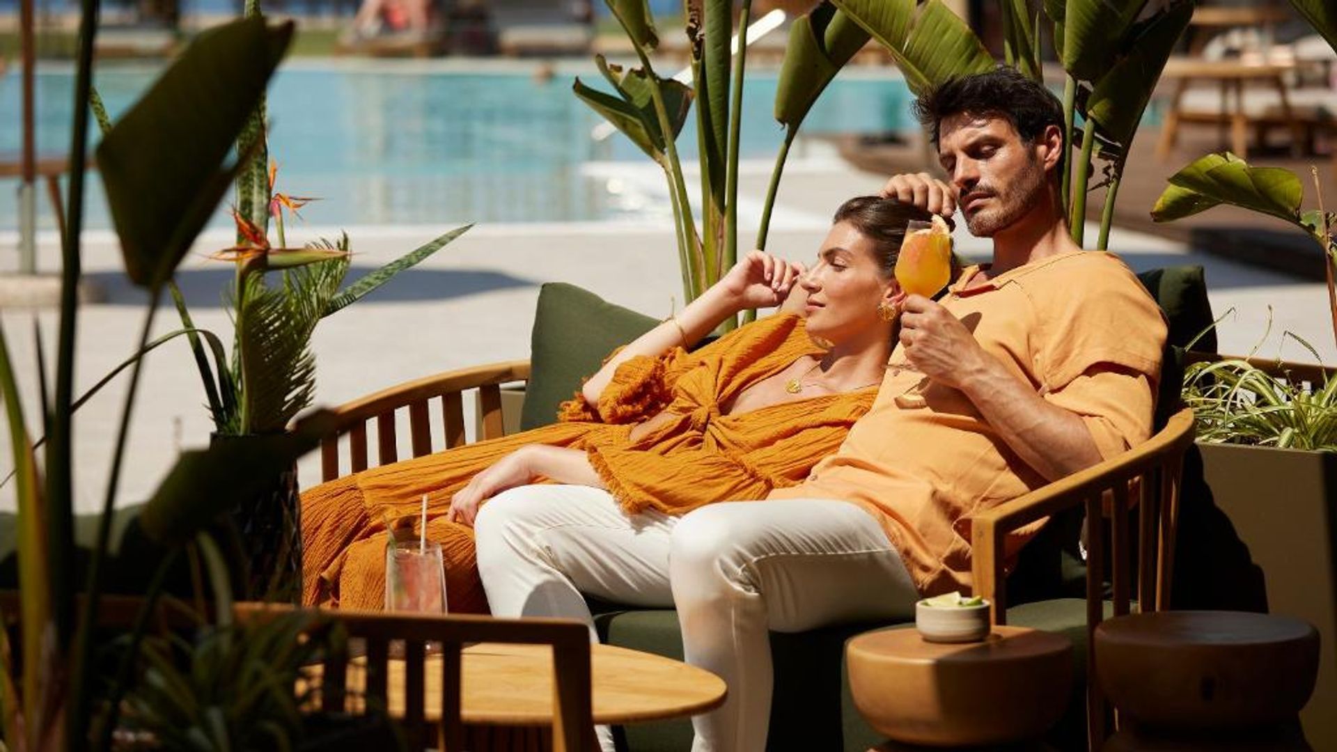 Pareja sentados en sillones de la piscina del Pareja tumbados en tumbonas del hotel Asterion Suites & Spa - Designed for Adults con una copa en la mano