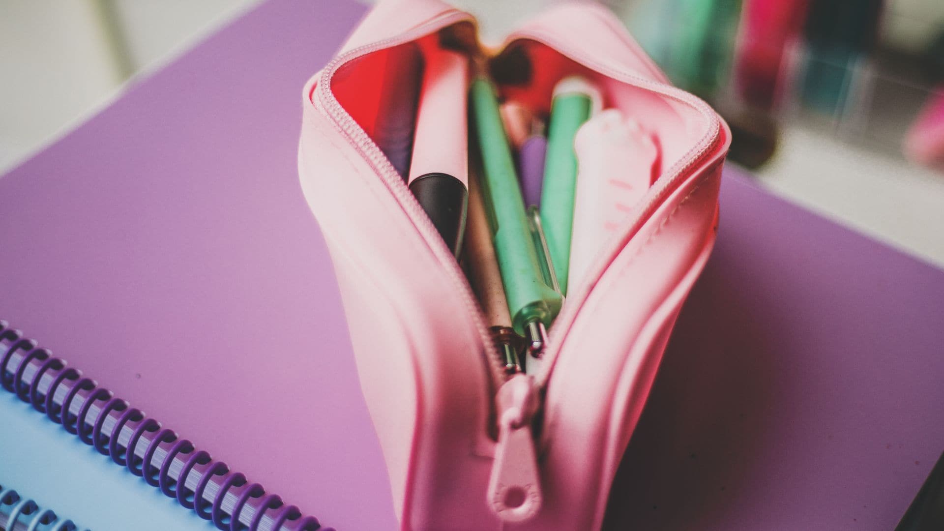 Estuche escolar en rosa abierto encima de unos cuadernos, con bolígrafos y subrayadores dentro.