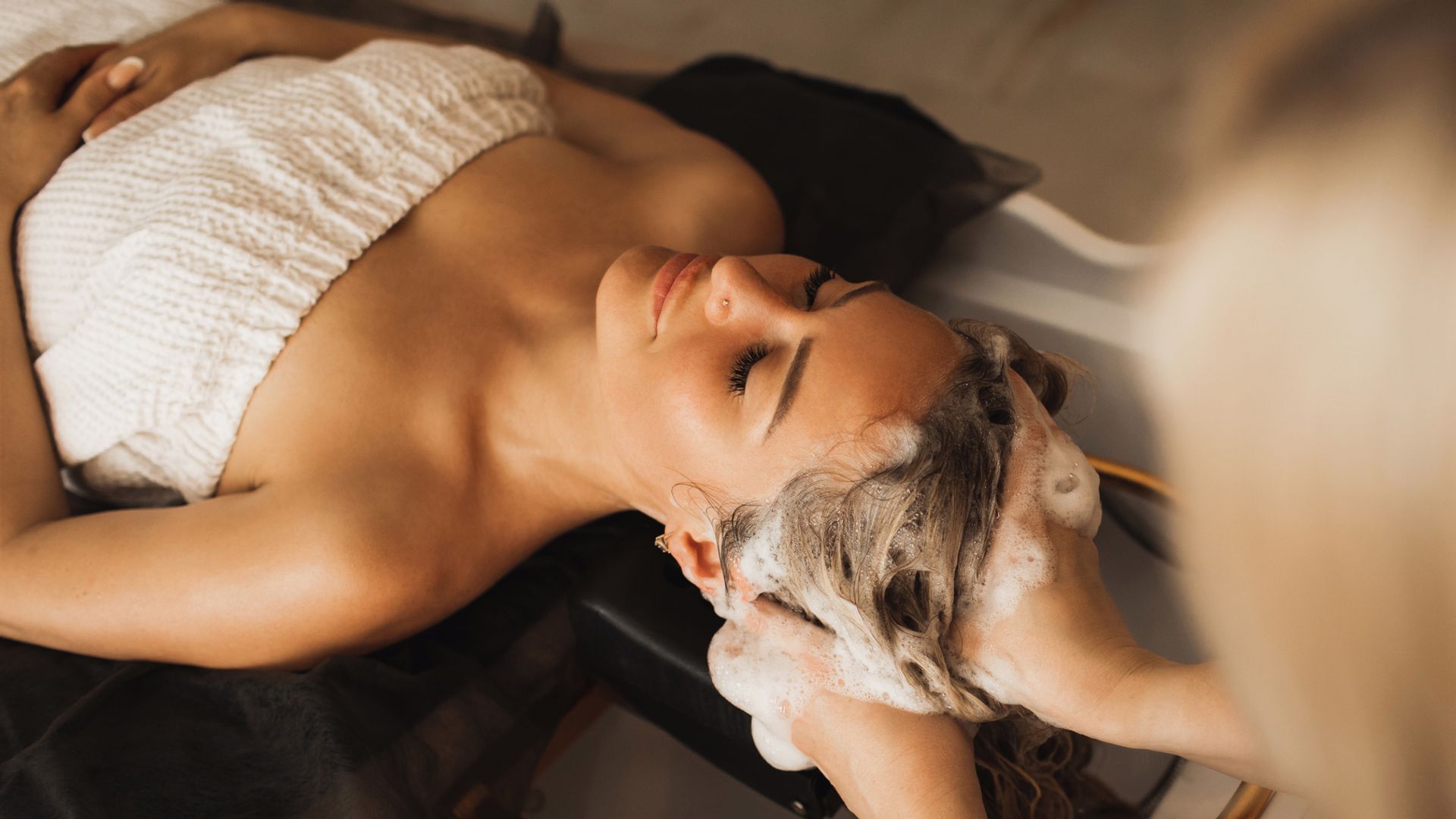 Mujer tumbada en salón de belleza relajada mientras le lavan el cabello