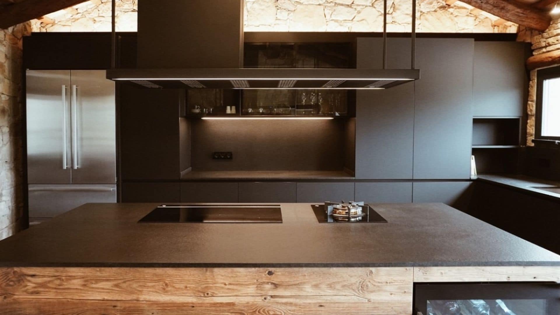 Cocina con muebles y encimera negros, campana decorativa de techo y vigas de madera