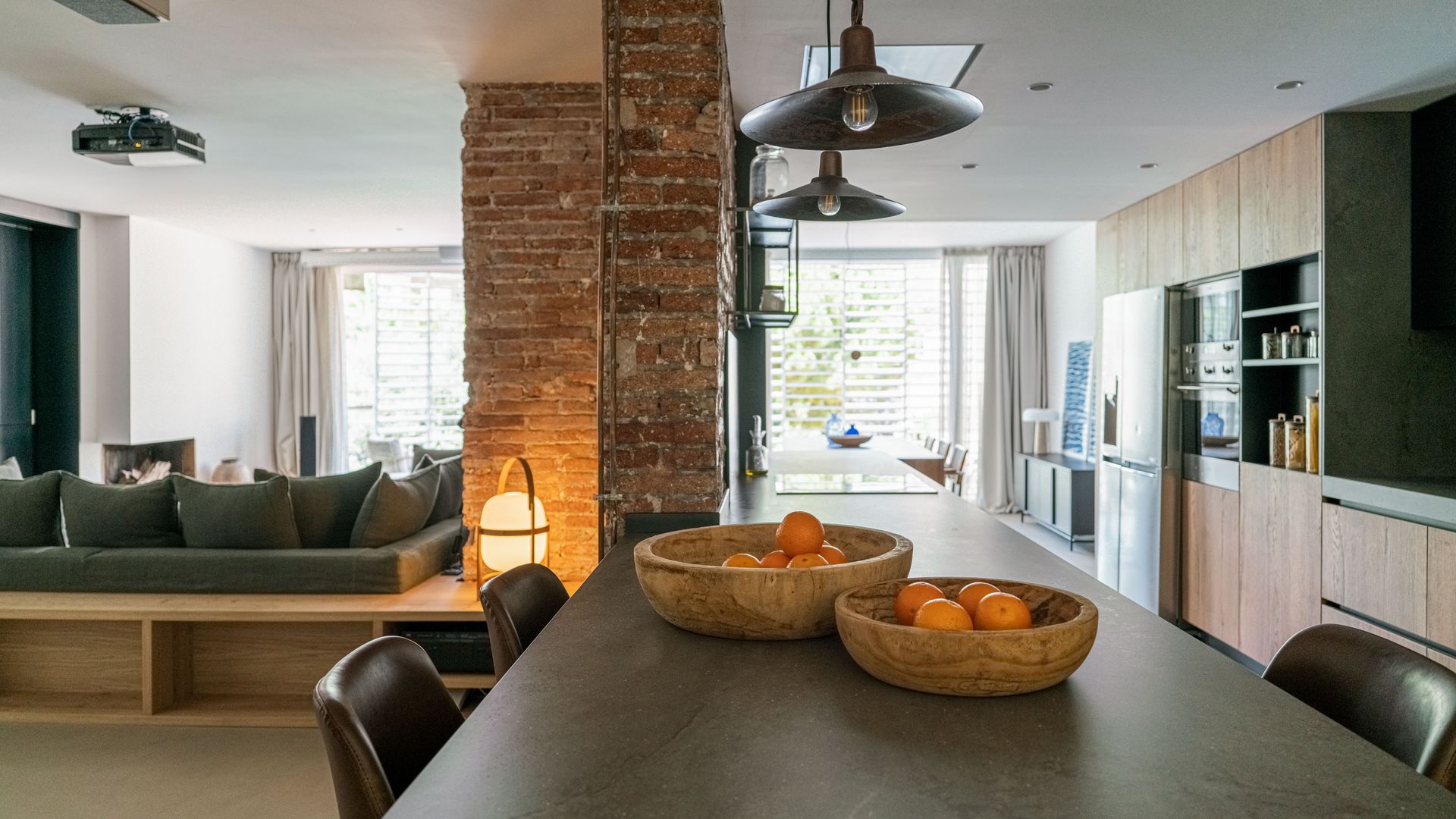 Salón comedor cocina con pared de ladrillo, mesa rectangular, lámparas de techo metálicas, lámpara Cesta