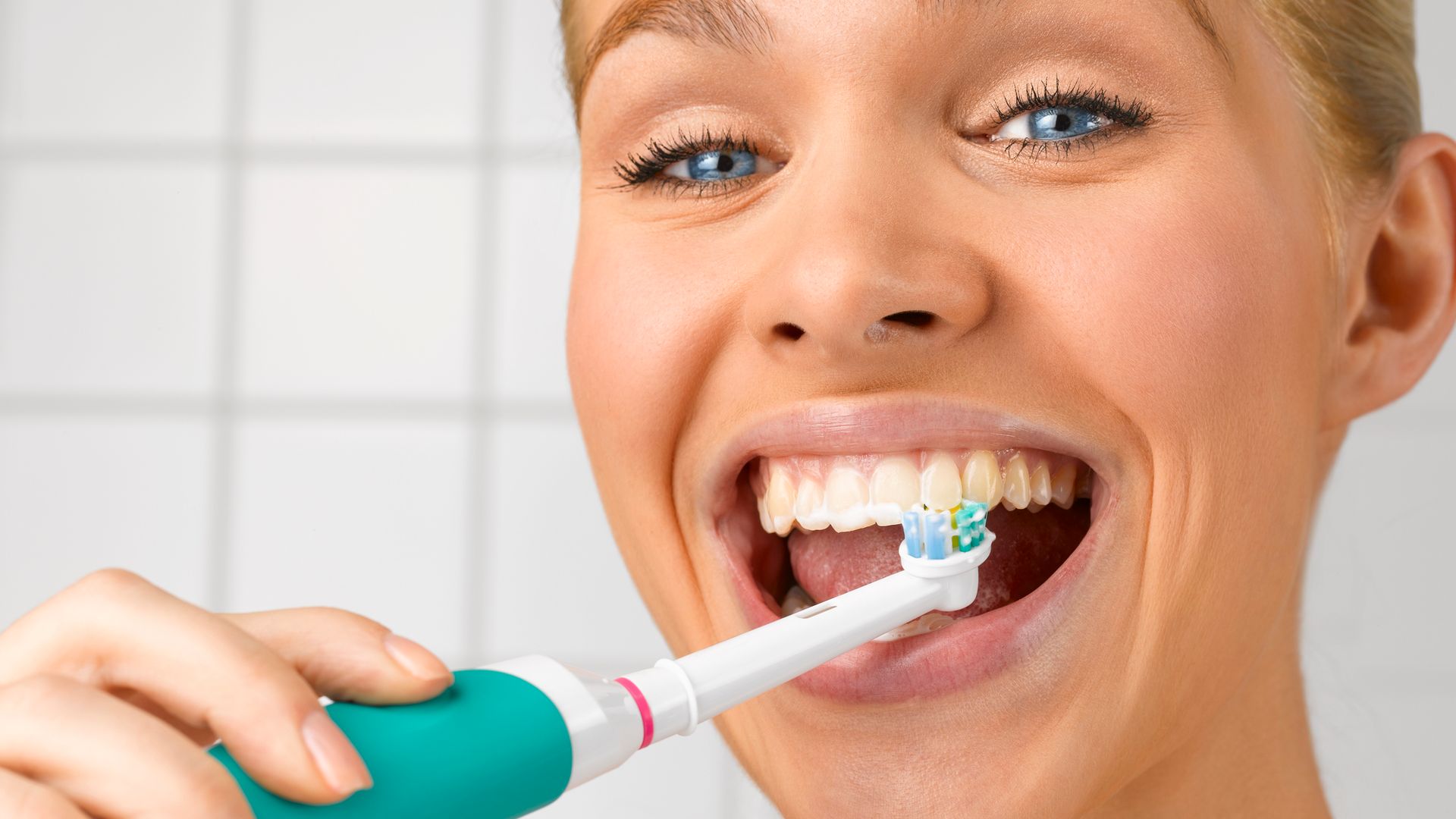 Mujer joven lavándose los dientes con un cepillo eléctrico.