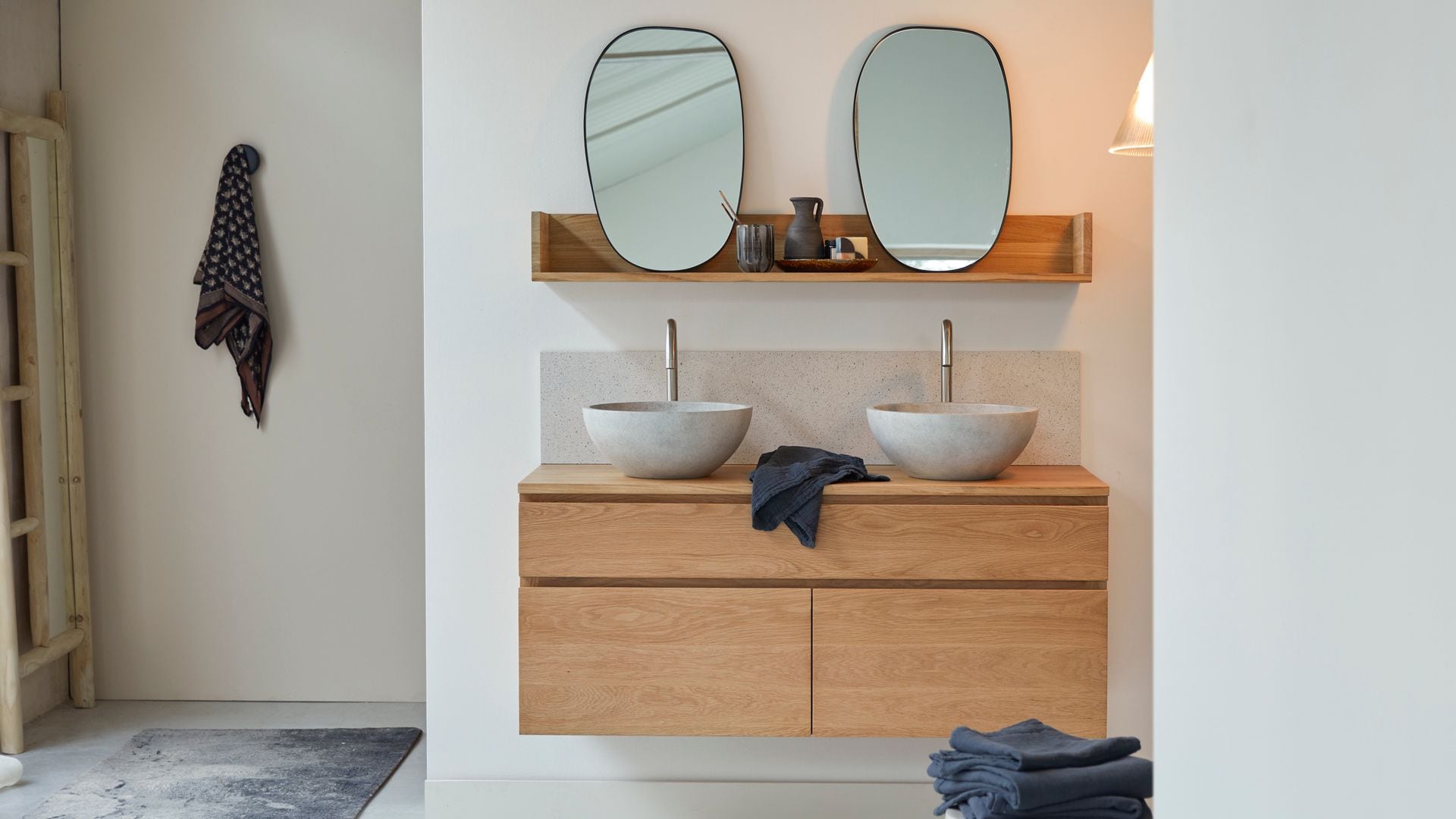 Baño con mueble bajolavabo de madera suspendido, dos lavabos redondos sobre la encimera, espejos ovalados y balda superior