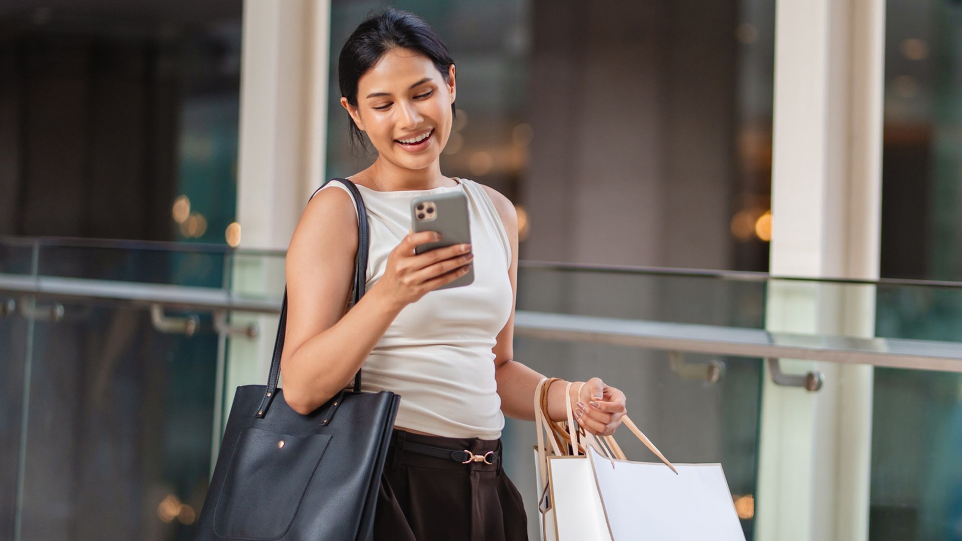 Mujer sonriente en un centro comercial con bolsas de compras mirando su teléfono móvil