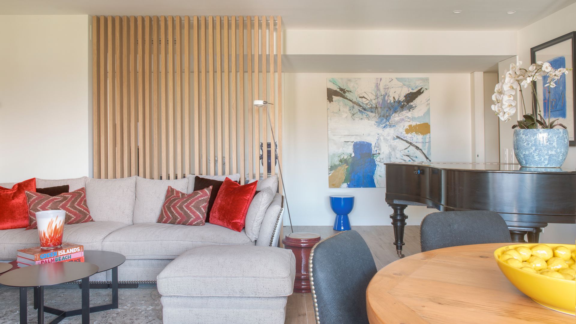 Salón con piano y tabique de lamas de madera separando el pasillo, sofá gris