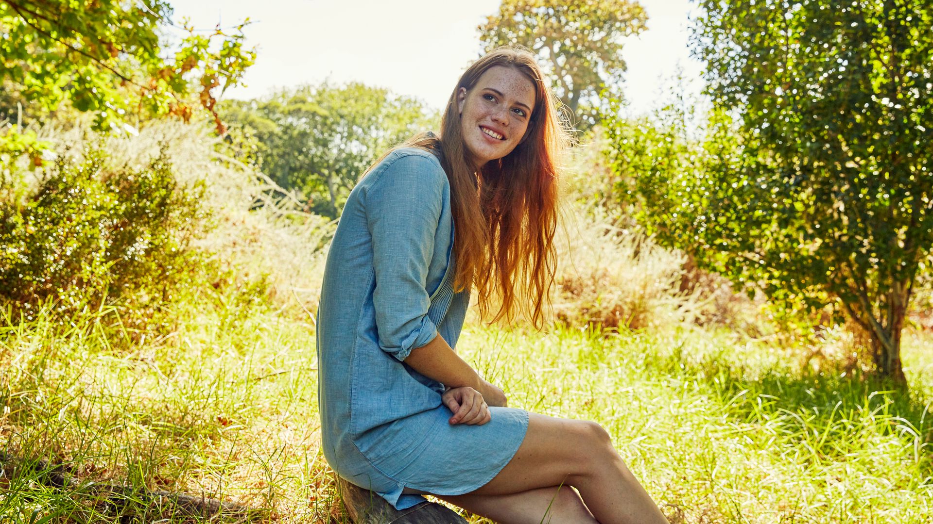 Retrato de una mujer sentada en el campo rodeada de árboles