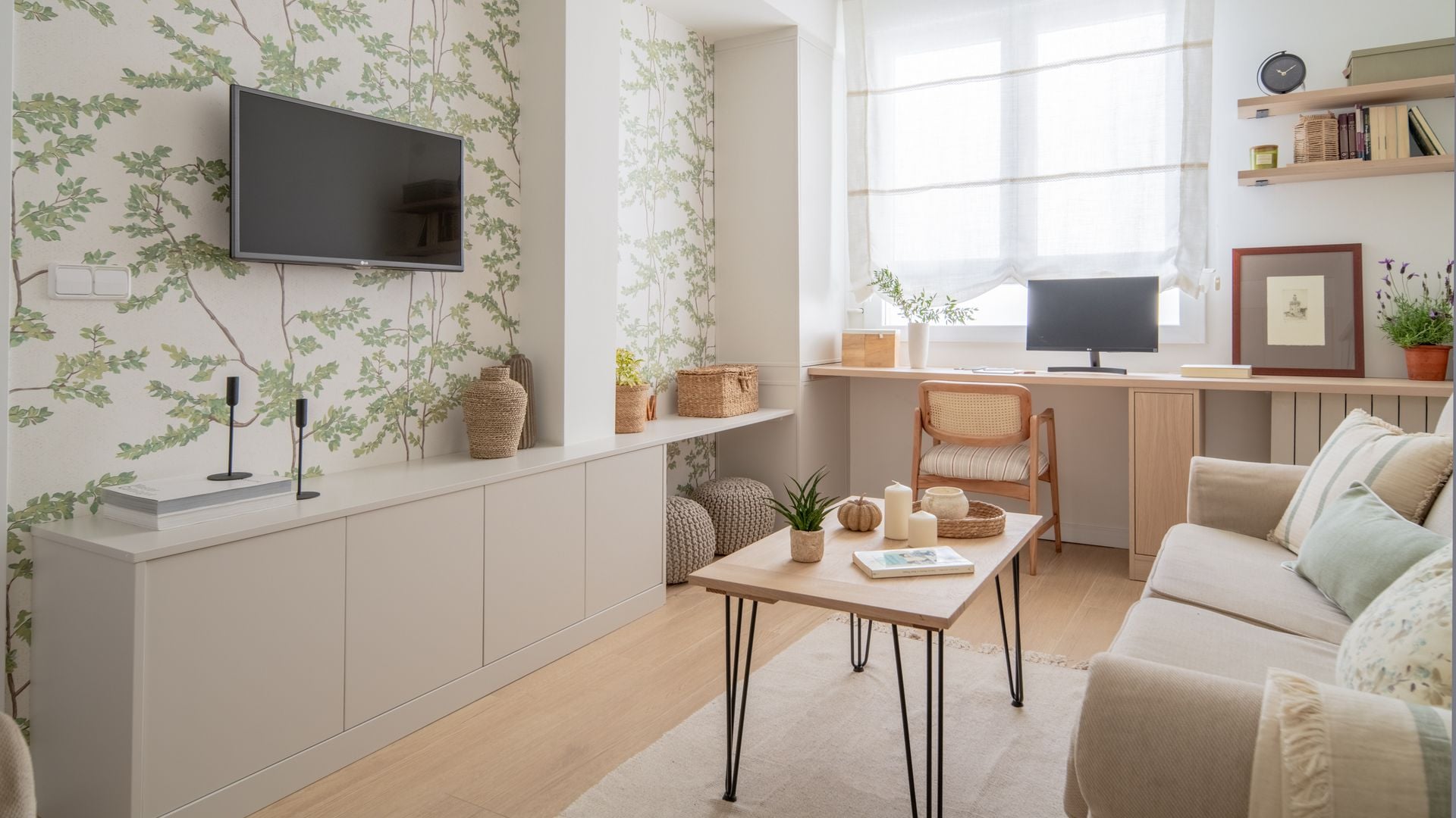 Salón con despacho, papel pintado en la pared de flores, televisión colgada en la pared, sofá beige, mesa de centro de madera, estores blancos, mueble a medida con espacio para dos pufs