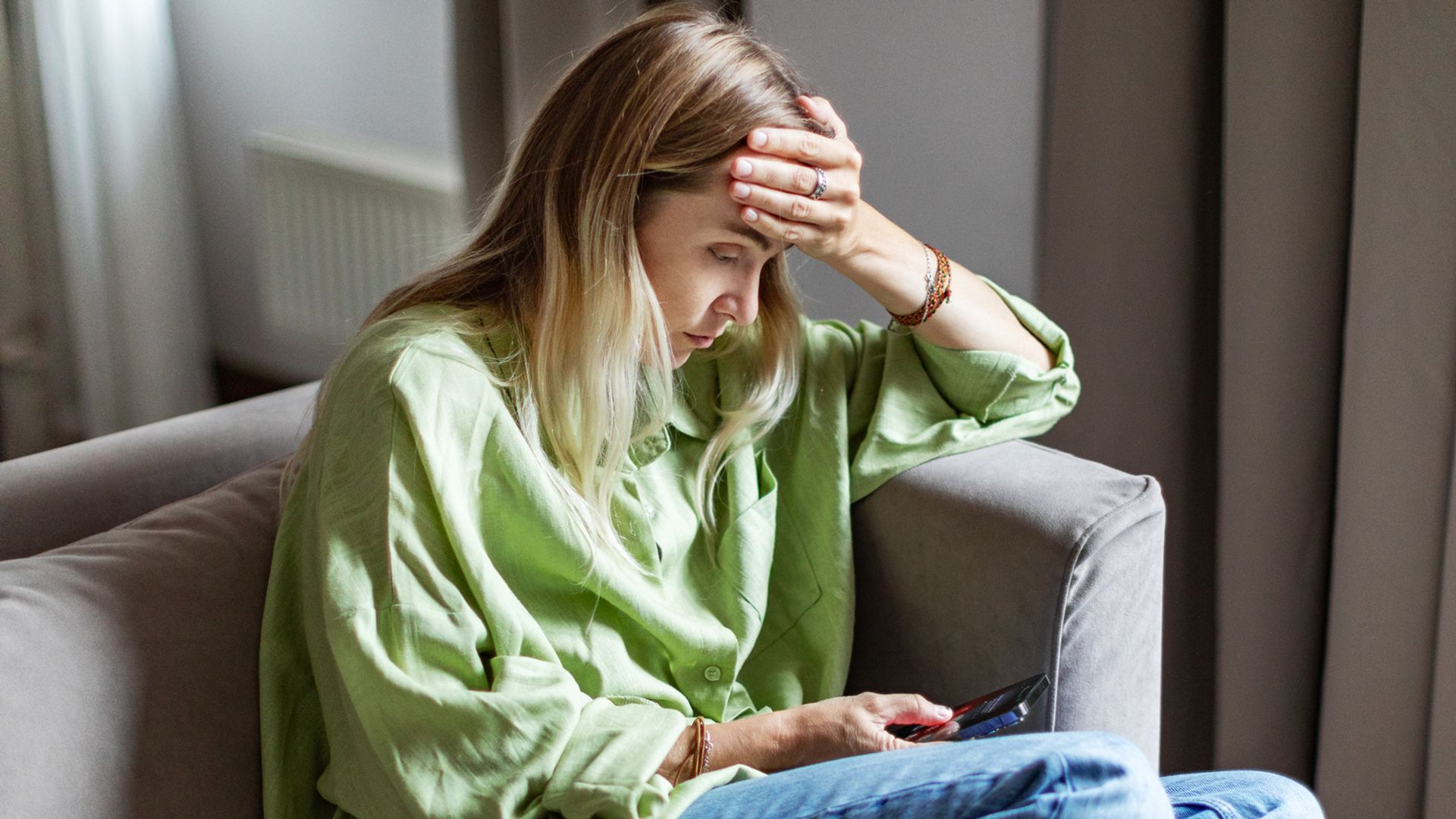 Mujer en un sofá preocupada mirando el móvil