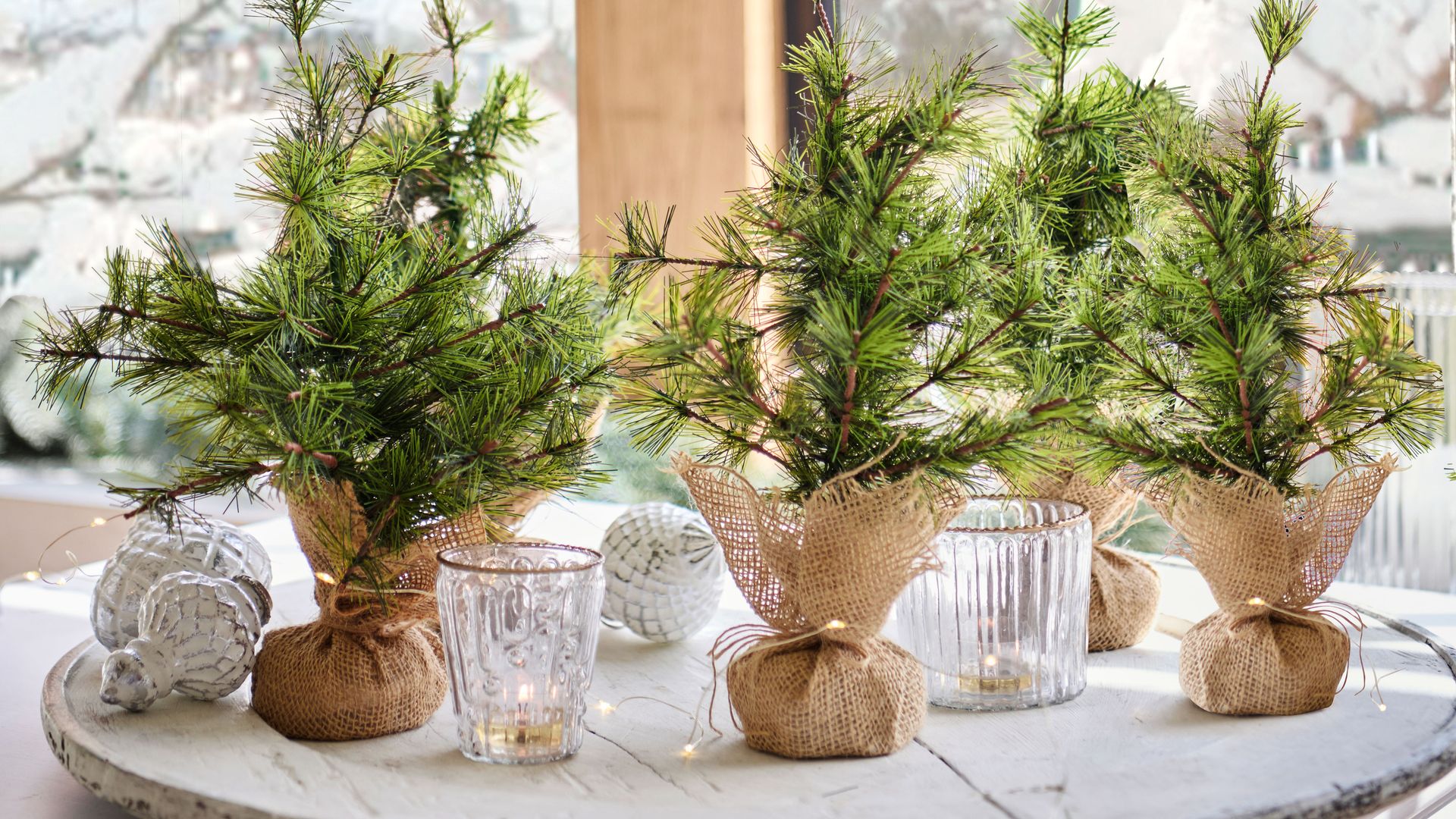 Centros de mesa navideños con tela de arpillera y ramas de abeto, guirnalda de luces, vasos 