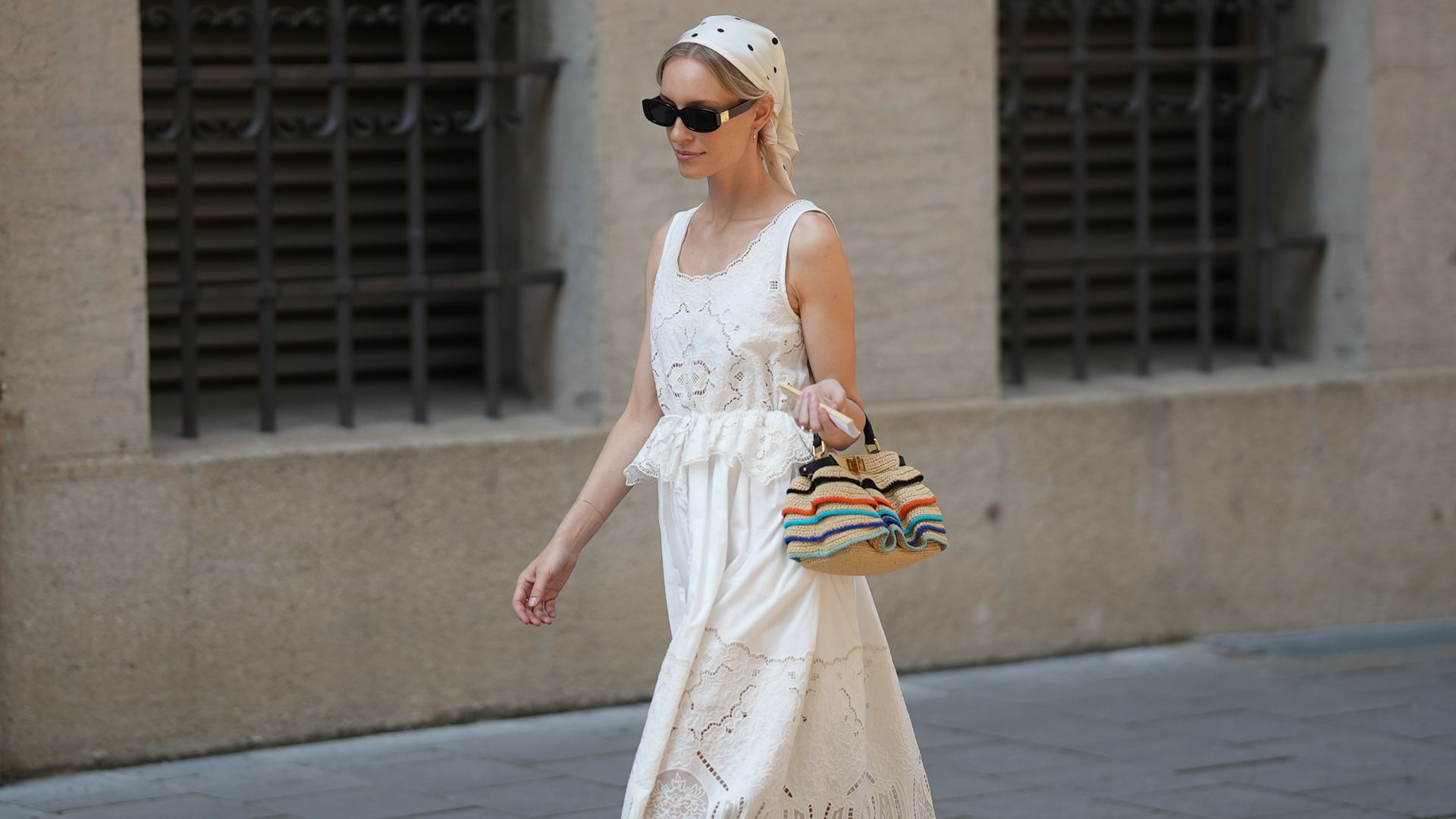 Mujer con vestido blanco con bordados, sandalias de dedo y bolso de rayas en Munich