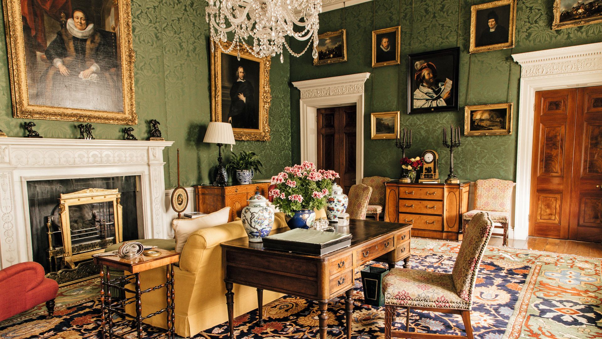 Sala elegante con escritorio, sofá, chimenea y retratos en las paredes.