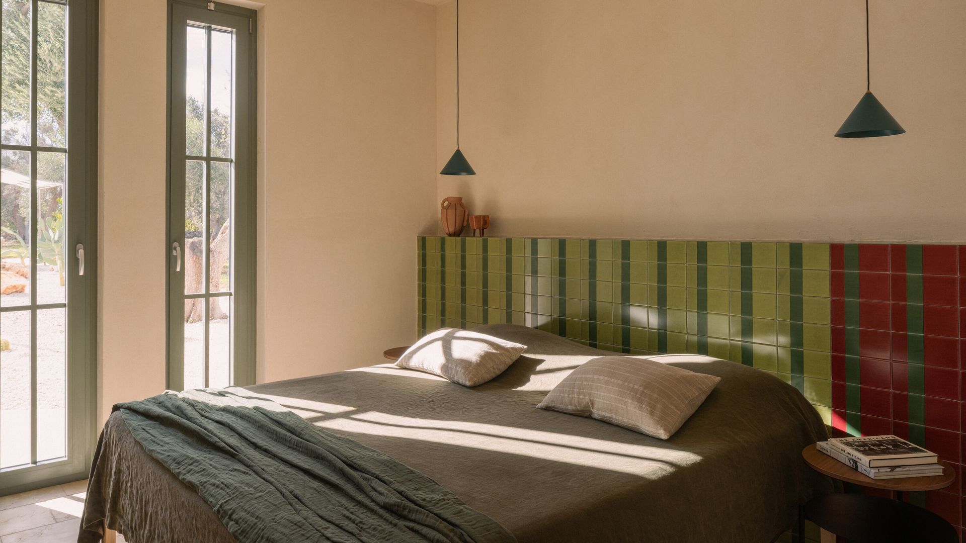 Dormitorio con cabecero de azulejos verdes y rojos, lámparas de techo a manos lados de la cama, salida al jardín 