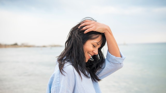 mujer sonriente tocando su cabello en la playa