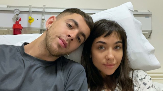 Plano medio de María Becerra y su novio, J Rei, acompañándola en una camilla de hospital