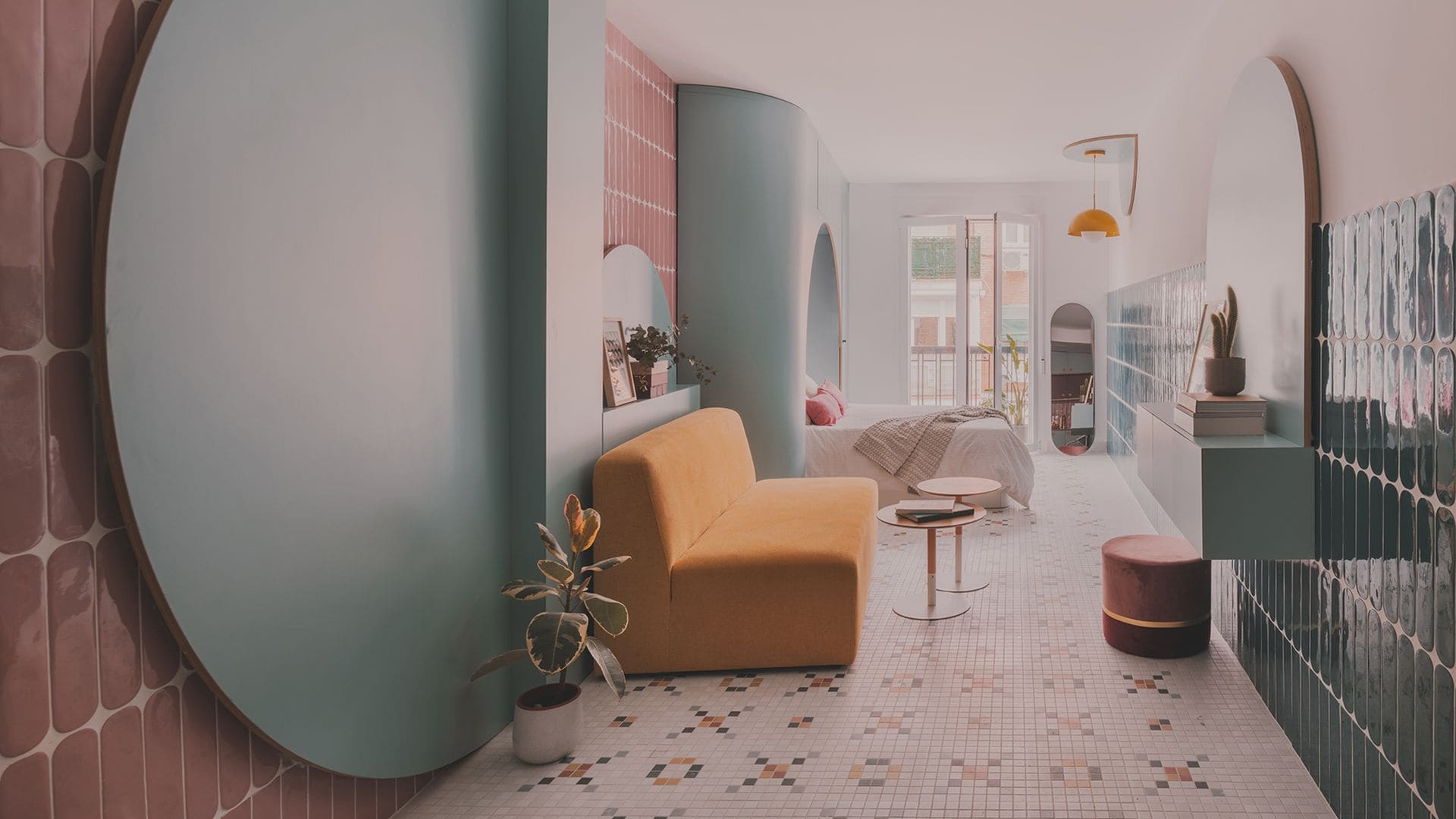 Espacio único con salón y dormitorio, paredes de azulejos de cerámica, suelo de cerámica, paneles circulares azules diferenciando las zonas, sofá amarillo, espejo y lámpara de techo amarilla 