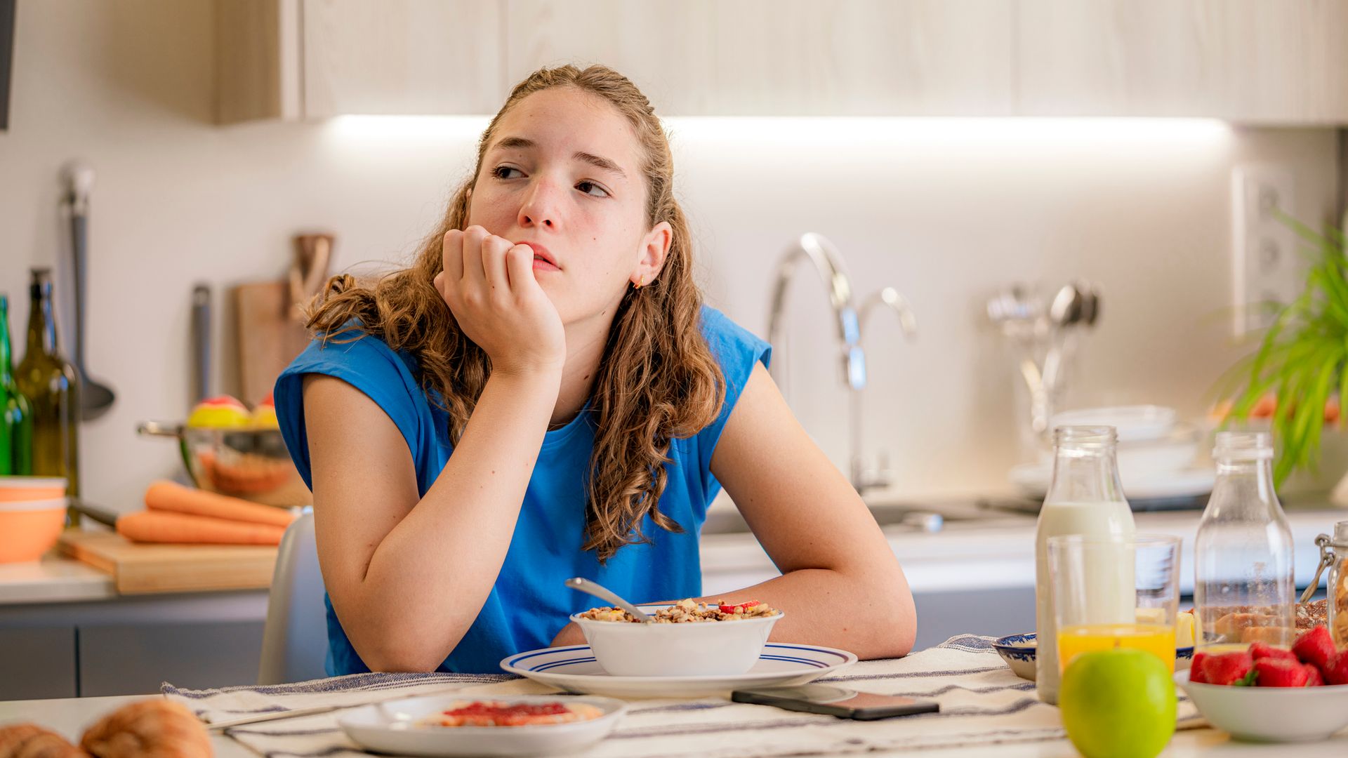 Adolescente pensativa, con el desayuno sobre la mesa